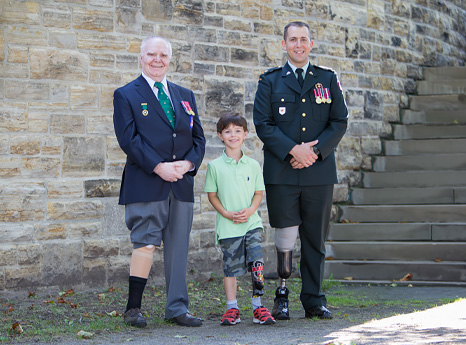 A young male leg amputee smiles and stands in between two male war amputee veterans.