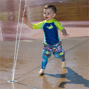 A young double leg amputee wearing his water legs while playing at a splash pad.