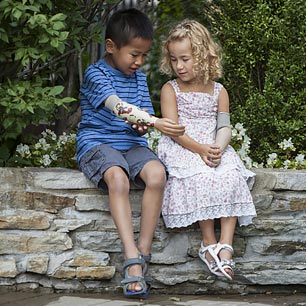 A boy and girl, both wearing artificial arms sitting on a stone ledge in a park.