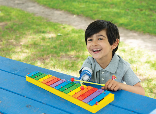 A young male arm amputee sits at a picnic table and plays a xylophone.