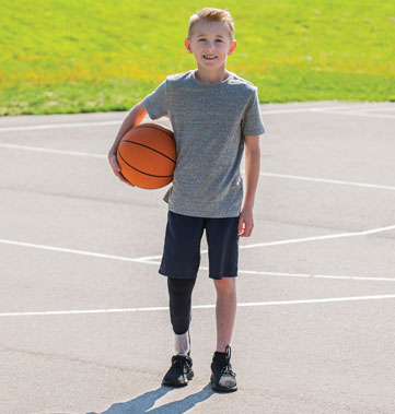 A young male leg amputee holds a basketball on a court.