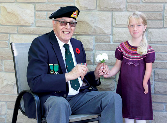 A young female arm amputee gives a white rose to an elderly Second World War amputee veteran wearing a uniform.