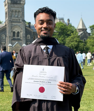 Un jeune homme amputé d’un bras est à l’extérieur et tient son diplôme universitaire.