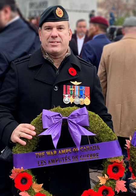 A male modern-day amputee veteran holds a War Amps wreath in front of Canada's National War Memorial.