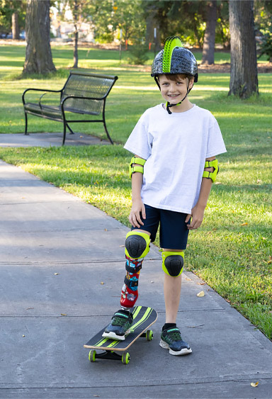 Un jeune garçon amputé d’une jambe fait de la planche à roulettes dans un parc.
