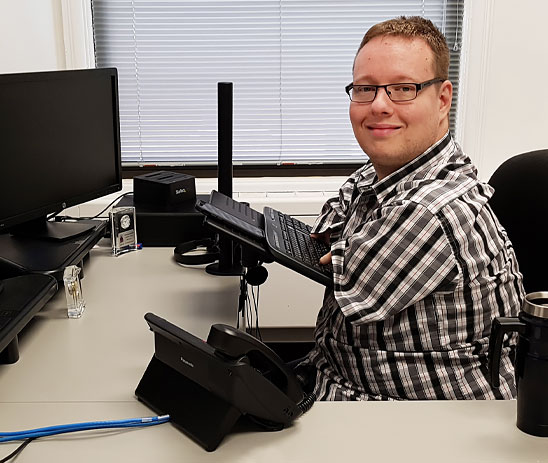A male adult multiple amputee uses an adaptive keyboard while sitting at his office desk.