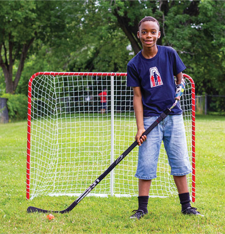 Un jeune garçon amputé d’un bras utilise un appareil pour le hockey et se tient debout devant un but de hockey sur un terrain.