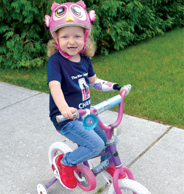 A young female multiple amputee smiles big while riding her bike.