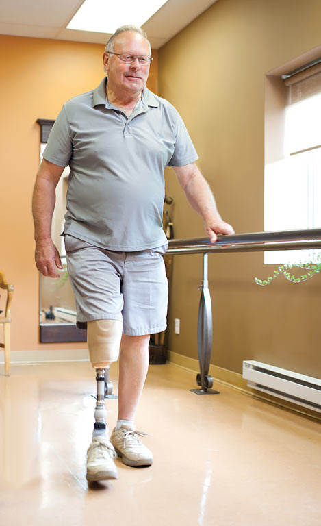 A male amputee wearing a prosthetic leg and walking alongside a parallel bar.