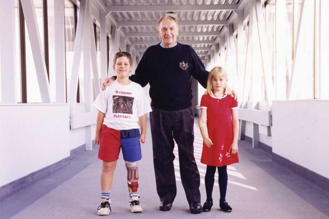 Cliff Chadderton stands between a young male leg amputee and a young female arm amputee.