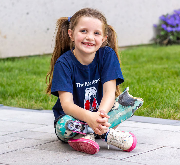 Michaela, a young double leg amputee, sits on a sidewalk.