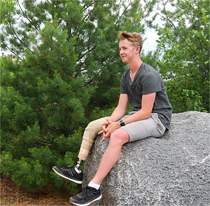 Champ Adam, a leg amputee, sitting on a large rock.