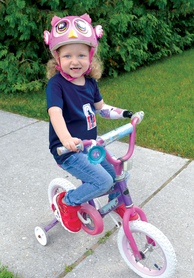 A young amputee girl using her artificial arm with a bike attachment to ride her bike.